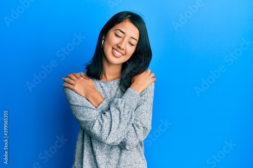 Beautiful asian young woman wearing casual clothes hugging oneself happy and positive, smiling confident. self love and self care