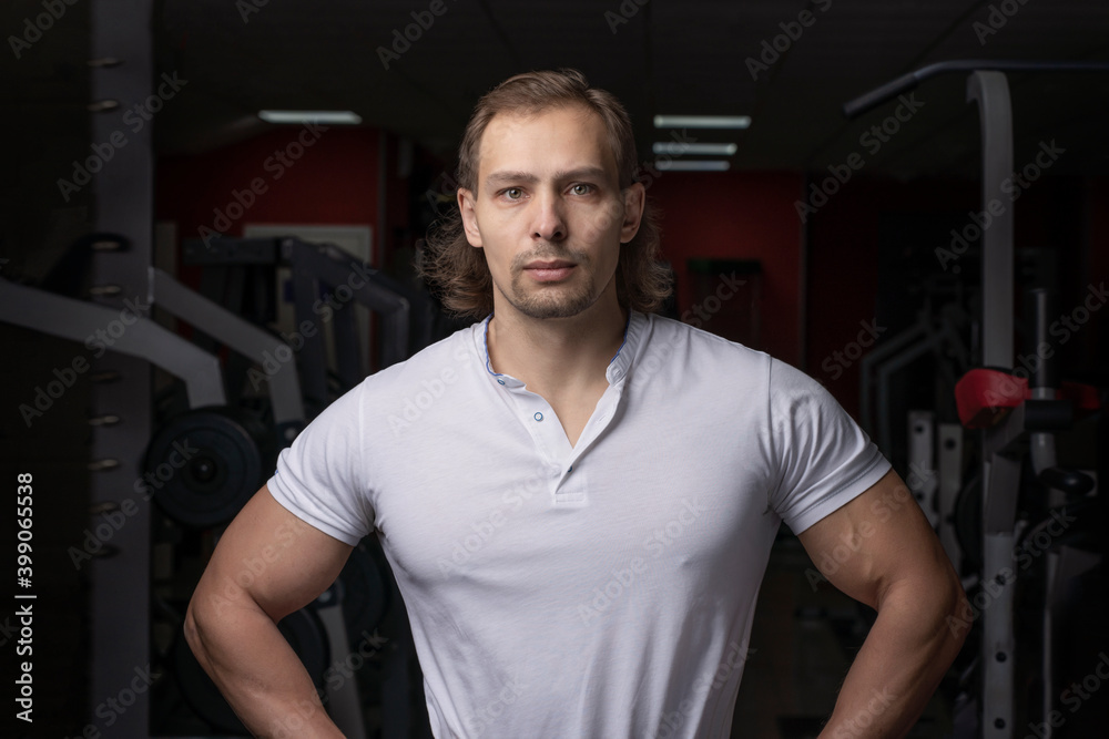 Personal trainer, portrait of a male athlete in a white shirt on the background of the gym