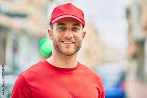 Young caucasian deliveryman smiling happy standing at the city.