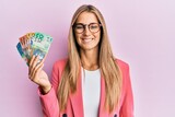Young blonde woman wearing business style holding australian dollars looking positive and happy standing and smiling with a confident smile showing teeth