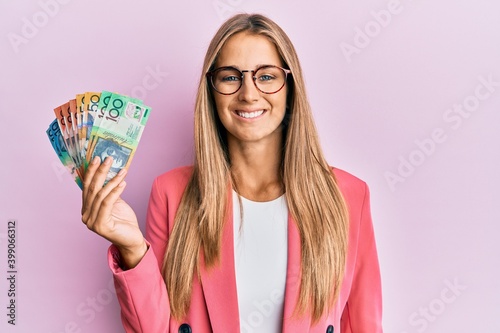 Young blonde woman wearing business style holding australian dollars looking positive and happy standing and smiling with a confident smile showing teeth