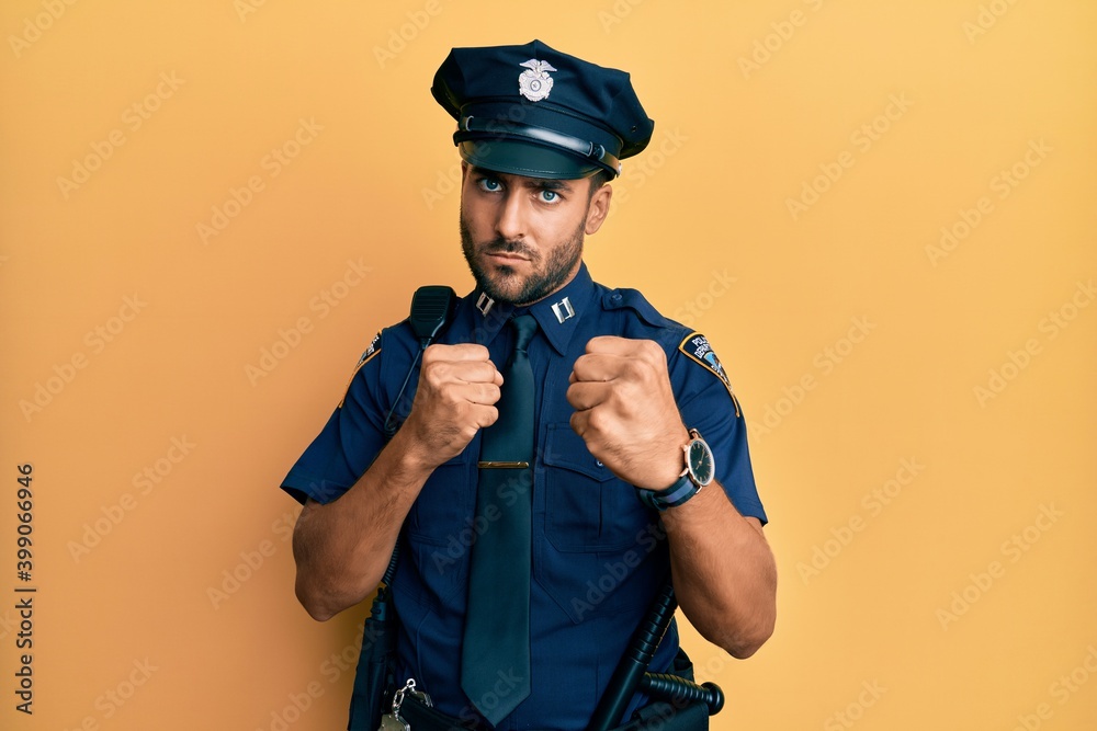 Handsome hispanic man wearing police uniform ready to fight with fist defense gesture, angry and upset face, afraid of problem Handsome hispanic man wearing police uniform ready to fight with fist defense gesture, angry and upset face, afraid of problem