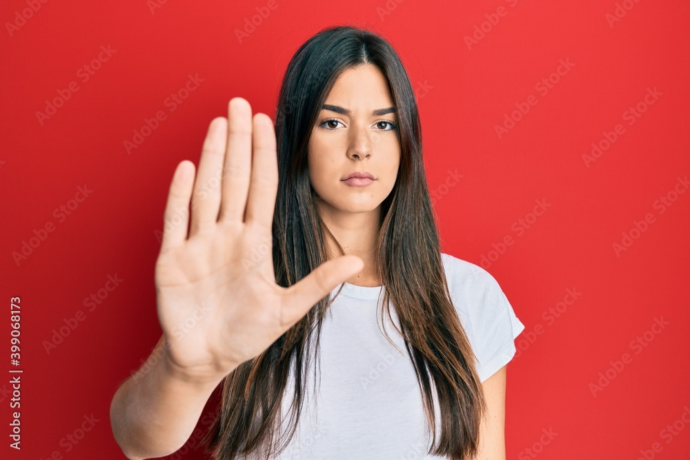 Young brunette woman wearing casual white tshirt over red background doing stop sing with palm of the hand. warning expression with negative and serious gesture on the face. Young brunette woman wearing casual white tshirt over red background doing stop sing with palm of the hand. warning expression with negative and serious gesture on the face.