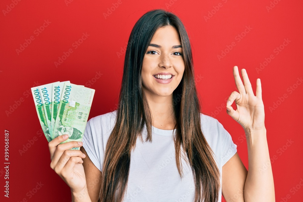 Young brunette woman holding 1000 south korean won banknotes doing ok sign with fingers, smiling friendly gesturing excellent symbol Young brunette woman holding 1000 south korean won banknotes doing ok sign with fingers, smiling friendly gesturing excellent symbol