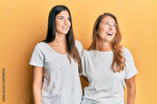 Hispanic family of mother and daughter wearing casual white tshirt looking away to side with smile on face, natural expression. laughing confident.
