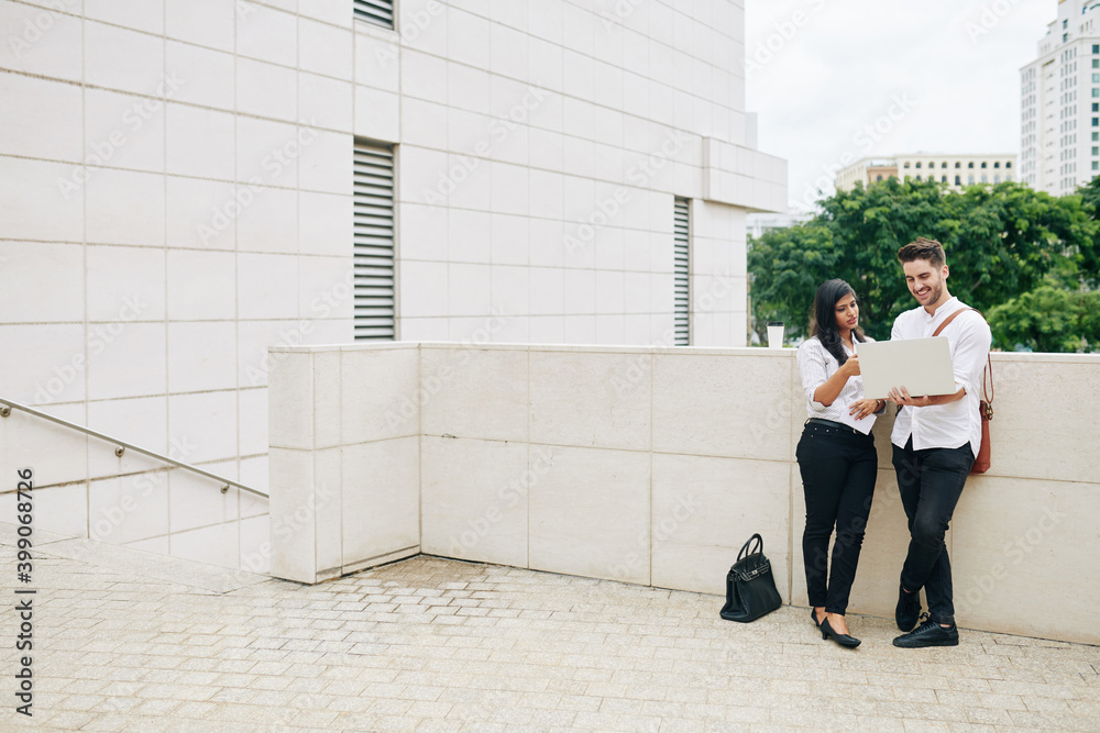 Multi-ethnic young business team standing outdoors with laptop an discussing last report or product presentation