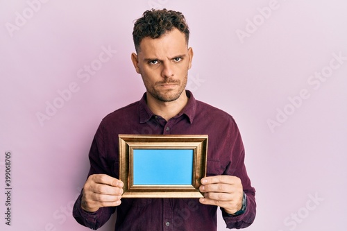 Obraz na plátne Young hispanic man holding empty frame skeptic and nervous, frowning upset because of problem