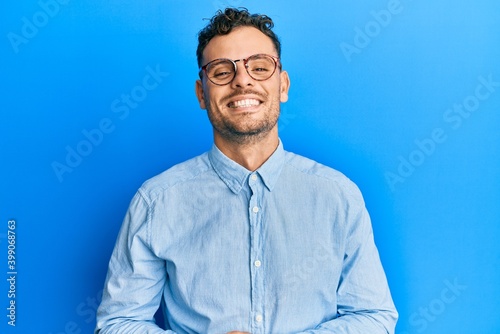 Young hispanic man wearing casual clothes and glasses with hands together and crossed fingers smiling relaxed and cheerful. success and optimistic