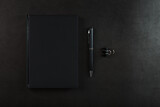 Black Notepad with a black pen on a black background.