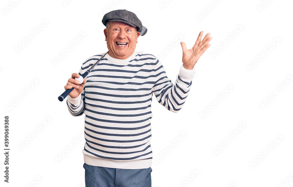 Senior handsome grey-haired man holding golf club and ball celebrating victory with happy smile and winner expression with raised hands Senior handsome grey-haired man holding golf club and ball celebrating victory with happy smile and winner expression with raised hands
