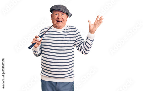 Senior handsome grey-haired man holding golf club and ball celebrating victory with happy smile and winner expression with raised hands