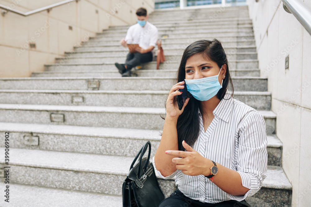 Φωτογραφία Pretty young emotional businesswoman in medical mask sitting on steps and talkin