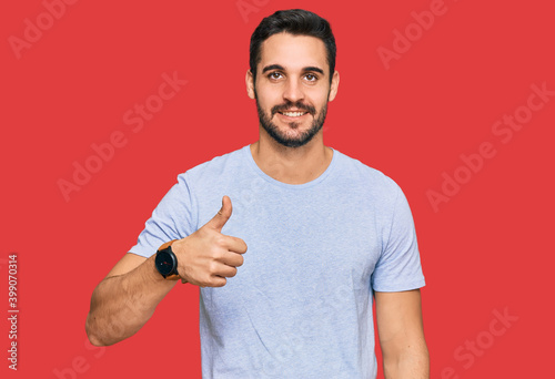 Young hispanic man wearing casual clothes doing happy thumbs up gesture with hand. approving expression looking at the camera showing success.