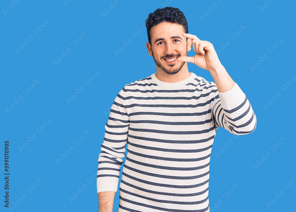 Fototapeta premium Young hispanic man wearing casual clothes smiling and confident gesturing with hand doing small size sign with fingers looking and the camera. measure concept.