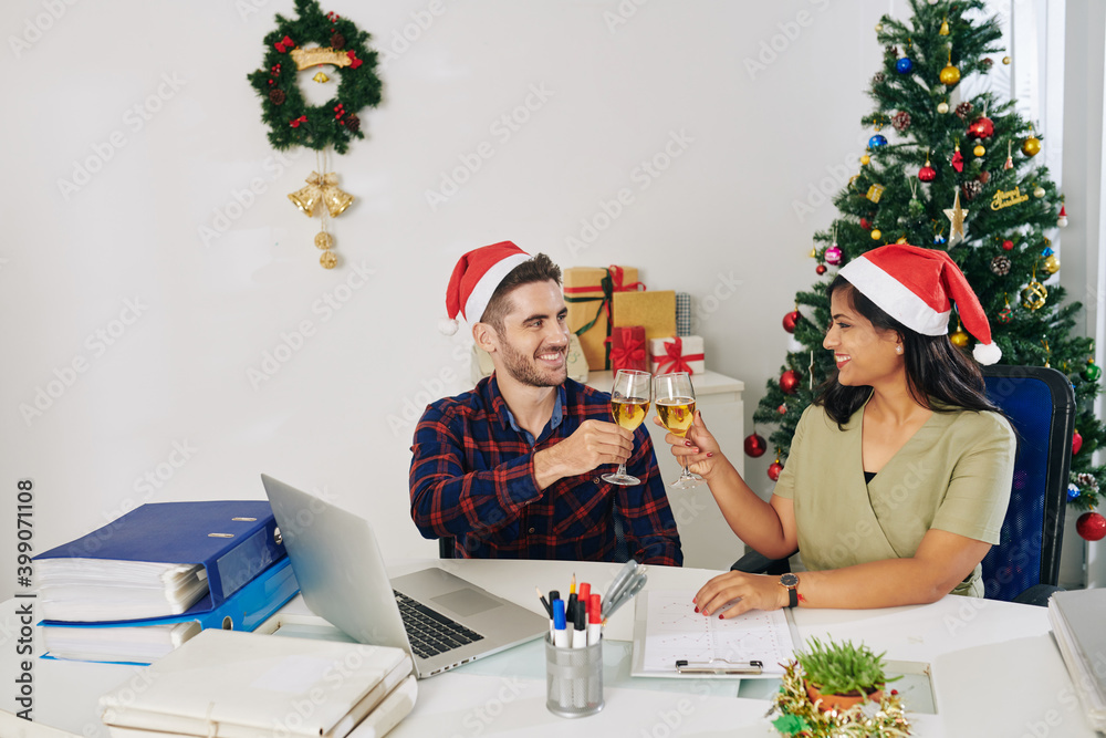 Fototapeta premium Young smiling colleagues celebrating Christmas in office and toasting with champagne glasses