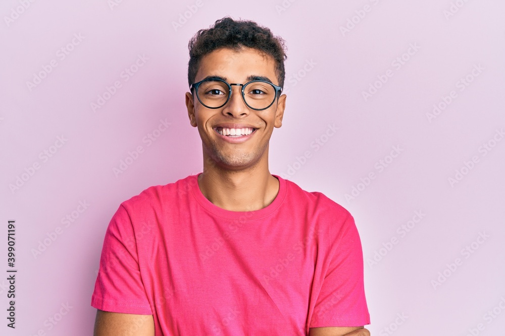 Young handsome african american man wearing glasses over pink background happy face smiling with crossed arms looking at the camera. positive person. - obrazy, fototapety, plakaty 