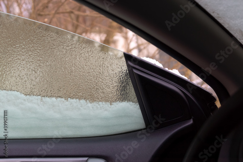 Snow on frozen window of a slightly opened car door in frosty winter