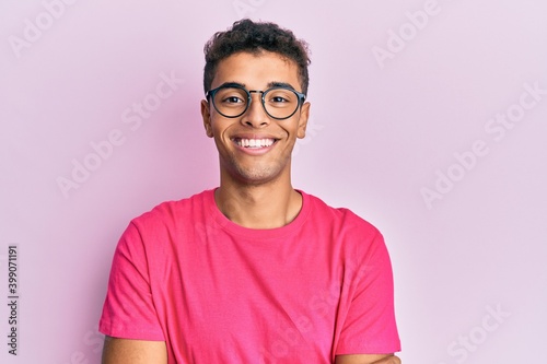Young handsome african american man wearing glasses over pink background happy face smiling with crossed arms looking at the camera. positive person.