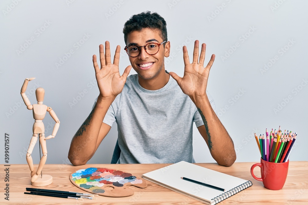Young handsome african american man painter sitting palette and art manikin showing and pointing up with fingers number ten while smiling confident and happy. Young handsome african american man painter sitting palette and art manikin showing and pointing up with fingers number ten while smiling confident and happy.