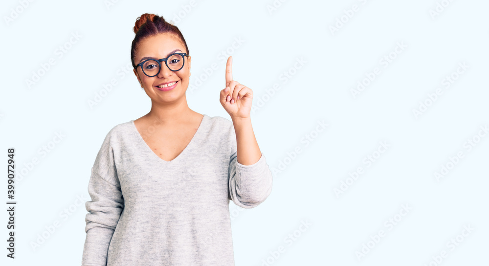 Young latin woman wearing casual clothes showing and pointing up with finger number one while smiling confident and happy. Young latin woman wearing casual clothes showing and pointing up with finger number one while smiling confident and happy.
