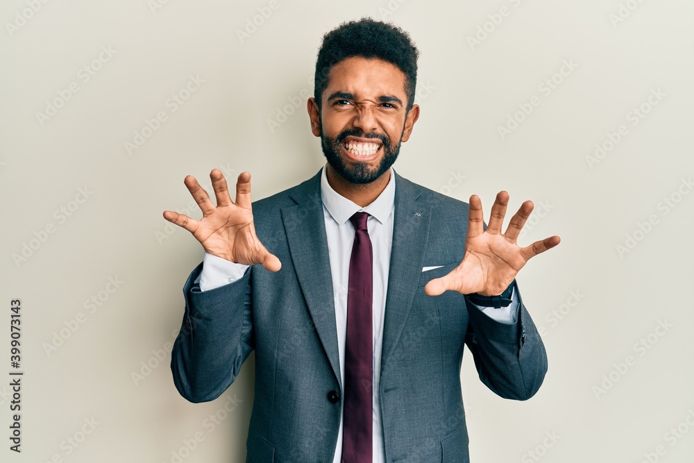 Handsome hispanic man with beard wearing business suit and tie smiling funny doing claw gesture as cat, aggressive and sexy expression Handsome hispanic man with beard wearing business suit and tie smiling funny doing claw gesture as cat, aggressive and sexy expression