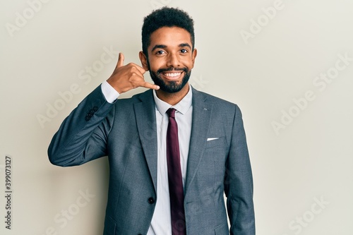Handsome hispanic man with beard wearing business suit and tie smiling doing phone gesture with hand and fingers like talking on the telephone. communicating concepts.