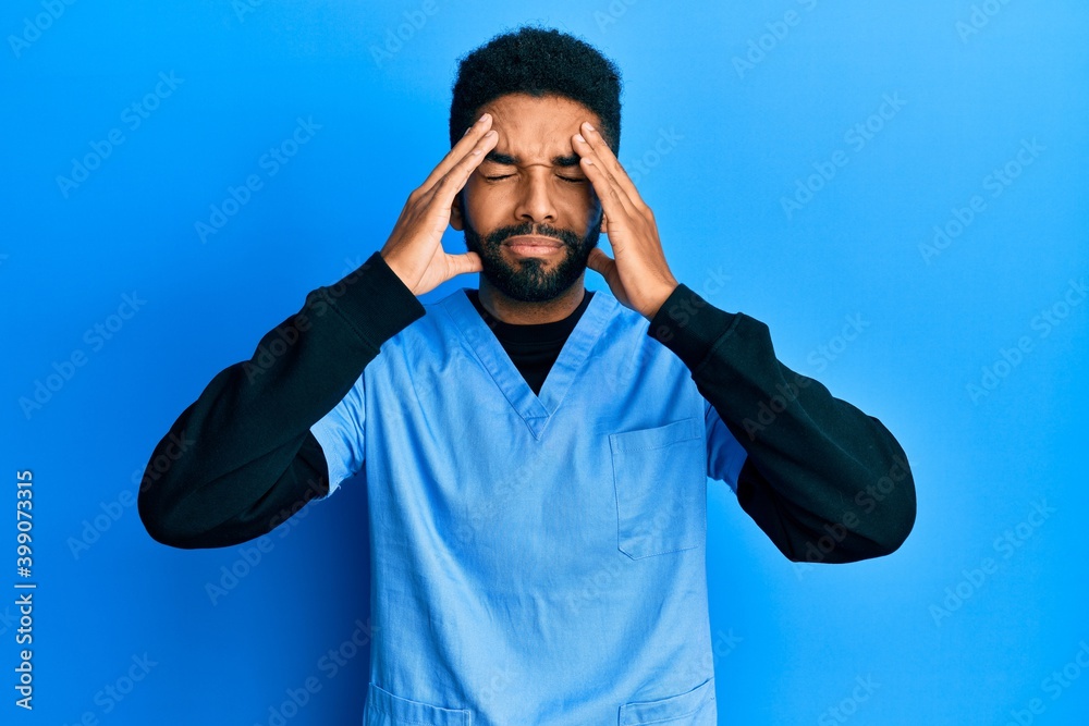 Handsome hispanic man with beard wearing blue male nurse uniform suffering from headache desperate and stressed because pain and migraine. hands on head. Handsome hispanic man with beard wearing blue male nurse uniform suffering from headache desperate and stressed because pain and migraine. hands on head.
