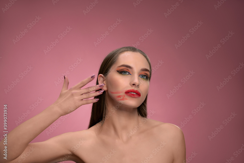 Messed up red lipstick on her face fashion model beautiful woman with long straight hair standing in the studio isolated on dirty pink background. Lips make up concept. 