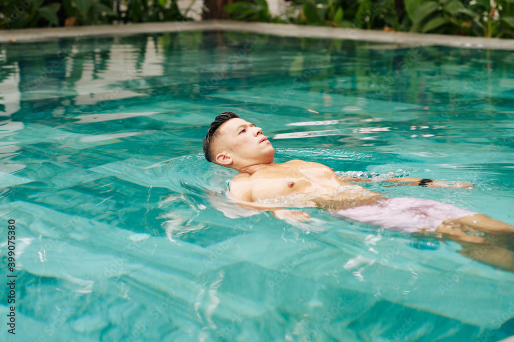 Handsome Asian man swimming in pool in the morning to get some refreshment on warm sunny day