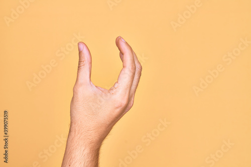 Hand of caucasian young man showing fingers over isolated yellow background picking and taking invisible thing  holding object with fingers showing space