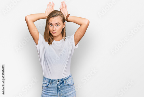 Beautiful young blonde woman wearing casual white t shirt doing bunny ears gesture with hands palms looking cynical and skeptical. easter rabbit concept. © Krakenimages.com