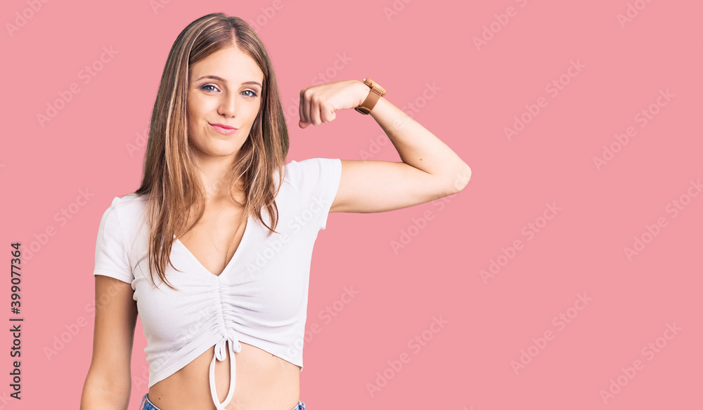 Naklejka premium Young beautiful blonde woman wearing casual white tshirt strong person showing arm muscle, confident and proud of power