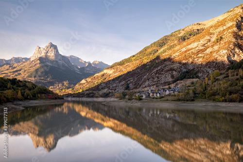 Mountain with water refllection in a lake with autumn tree forest and a small town in Aragon, Heusca, Spain