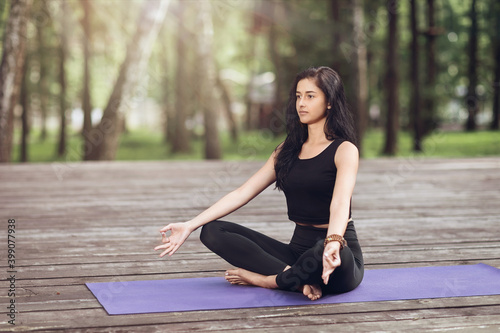 Young woman in sportswear practicing yoga asanas and meditating in the park on a wooden bridge on a summer morning © Sergey Chayko