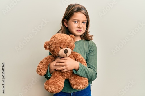 Little beautiful girl hugging teddy bear clueless and confused expression. doubt concept.