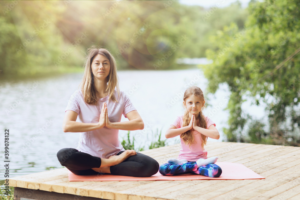 Mom and daughter practice yoga asanas on the river bank on a warm sunny day. Healthy lifestyle concept Mom and daughter practice yoga asanas on the river bank on a warm sunny day. Healthy lifestyle concept