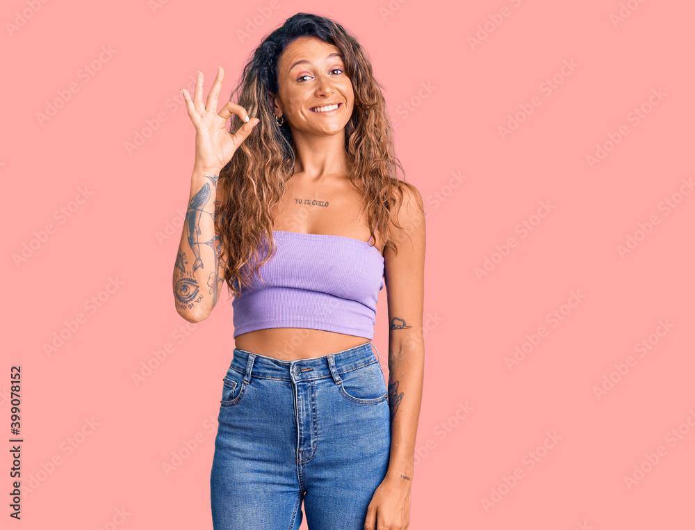 Young hispanic woman with tattoo wearing casual clothes smiling positive doing ok sign with hand and fingers. successful expression. Young hispanic woman with tattoo wearing casual clothes smiling positive doing ok sign with hand and fingers. successful expression.