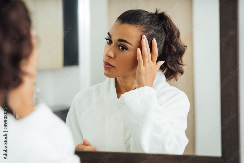 Beautiful brunette looking at reflection in the mirror and touching hair Beautiful brunette looking at reflection in the mirror and touching hair