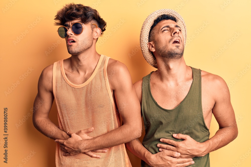 Young gay couple wearing summer clothes with hand on stomach because nausea, painful disease feeling unwell. ache concept. Young gay couple wearing summer clothes with hand on stomach because nausea, painful disease feeling unwell. ache concept.