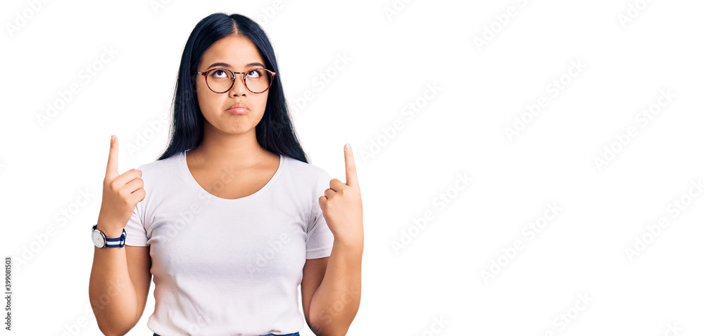 Young beautiful asian girl wearing casual clothes and glasses pointing up looking sad and upset, indicating direction with fingers, unhappy and depressed. Young beautiful asian girl wearing casual clothes and glasses pointing up looking sad and upset, indicating direction with fingers, unhappy and depressed.
