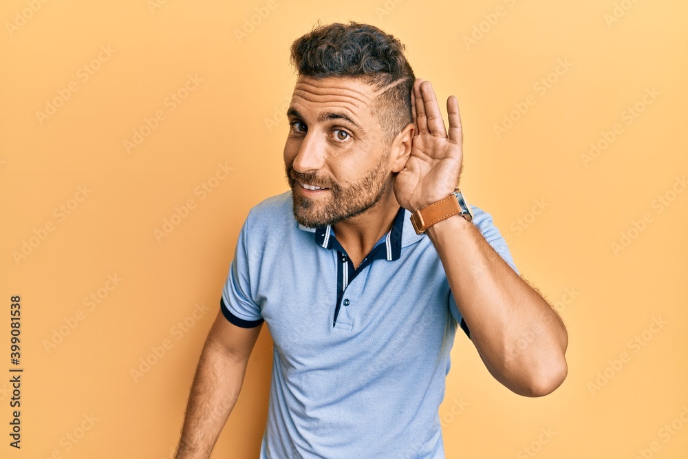 Handsome man with beard wearing casual clothes smiling with hand over ear listening an hearing to rumor or gossip. deafness concept.