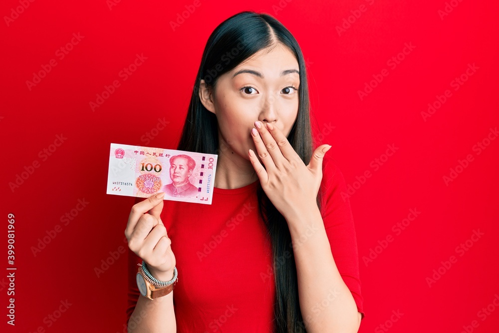 Young chinese woman holding 100 yuan chinese banknote covering mouth with hand, shocked and afraid for mistake. surprised expression Young chinese woman holding 100 yuan chinese banknote covering mouth with hand, shocked and afraid for mistake. surprised expression