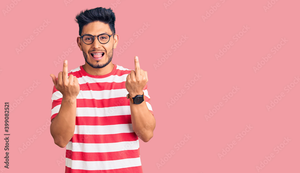 Handsome latin american young man wearing casual clothes and glasses showing middle finger doing fuck you bad expression, provocation and rude attitude. screaming excited Handsome latin american young man wearing casual clothes and glasses showing middle finger doing fuck you bad expression, provocation and rude attitude. screaming excited