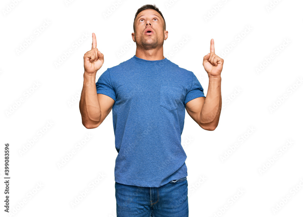 Handsome muscle man wearing casual clothes amazed and surprised looking up and pointing with fingers and raised arms. Handsome muscle man wearing casual clothes amazed and surprised looking up and pointing with fingers and raised arms.