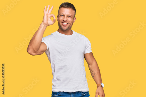 Handsome muscle man wearing casual white tshirt smiling positive doing ok sign with hand and fingers. successful expression.