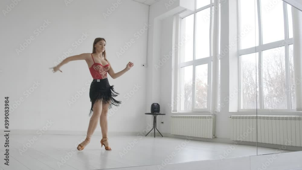 Attractive girl dances ballroom dancing in front of a mirror in a bright white hall. A professional ballroom dancer trains in a choreographic hall. Attractive girl dances ballroom dancing in front of a mirror in a bright white hall. A professional ballroom dancer trains in a choreographic hall.