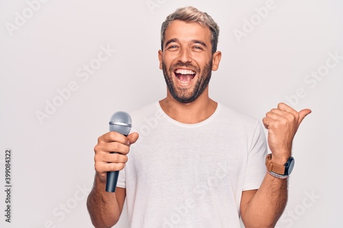 Handsome blond singer man with beard singing song using microphone over white background pointing thumb up to the side smiling happy with open mouth