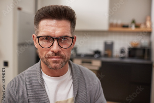 Portrait of handsome mature man wearing glasses and looking at camera with serious face expression while sitting in kitchen interior at home, copy space