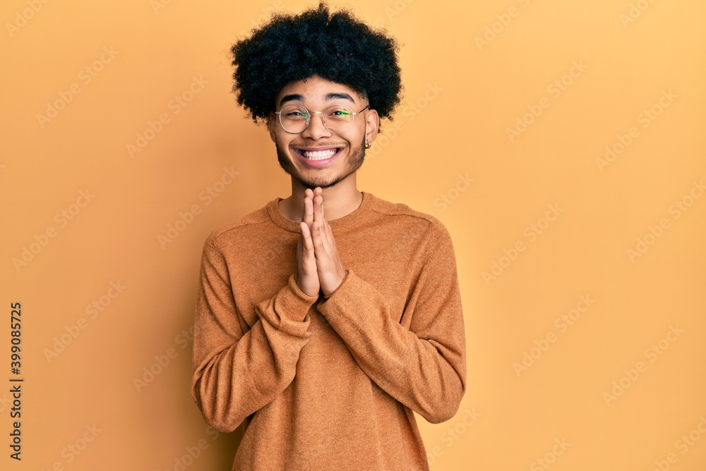 Young african american man with afro hair wearing casual winter sweater praying with hands together asking for forgiveness smiling confident. Young african american man with afro hair wearing casual winter sweater praying with hands together asking for forgiveness smiling confident.