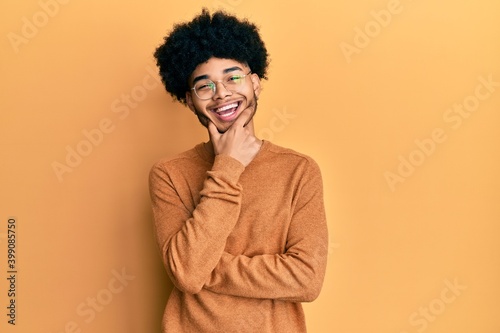 Young african american man with afro hair wearing casual winter sweater looking confident at the camera smiling with crossed arms and hand raised on chin. thinking positive.